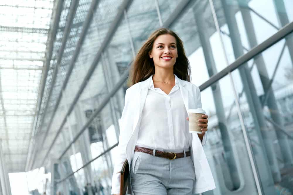 Woman in a business casual attire holding a cup of coffee on her way to work.