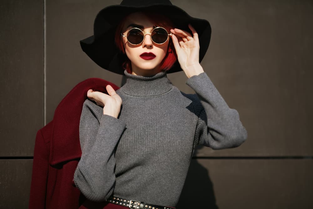Female model wearing stylish wide-brimmed hat, sunglasses, and a turtleneck top.