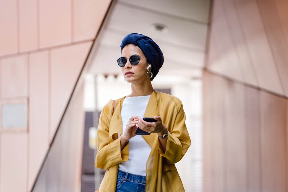 Woman in a modest style outfit listening to music via wireless earphones.