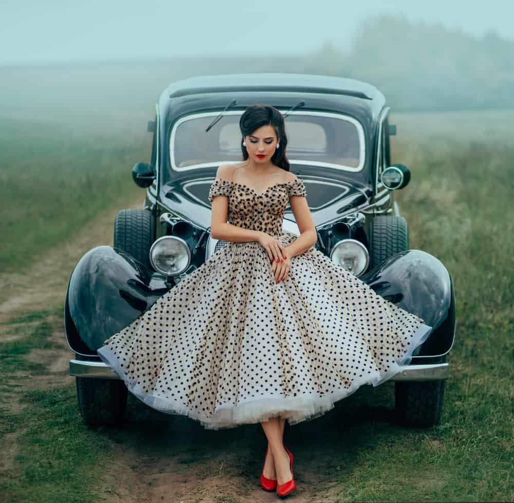 Model in pin up style clothes posing against a black retro car.