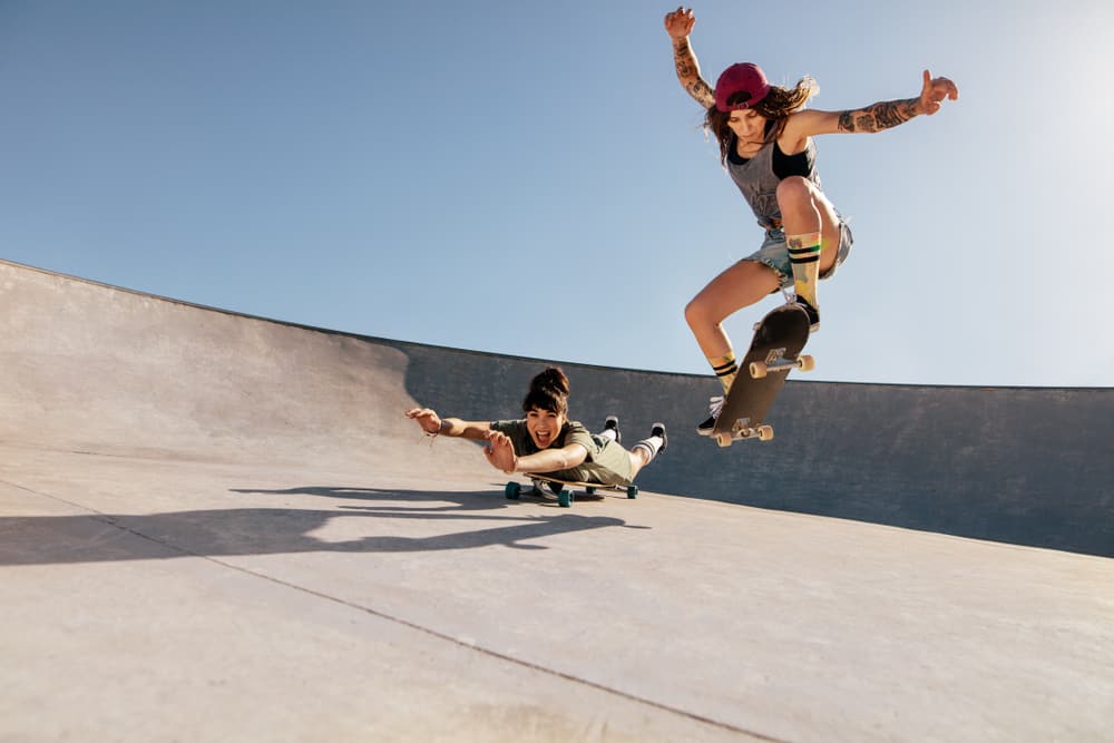 Two women doing stunts on skateboards at a skate park.