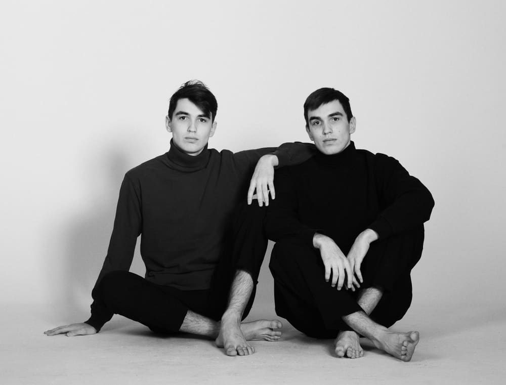 Black and white photo of two men wearing black sweaters.
