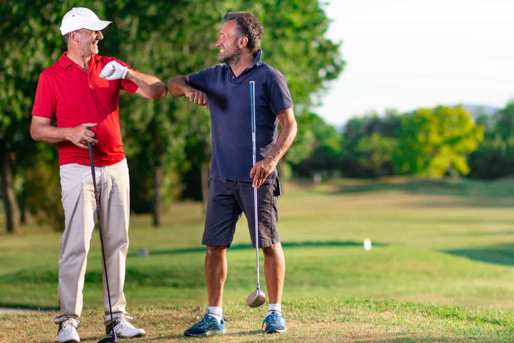 Two golf friends greet each other by touching their elbows.