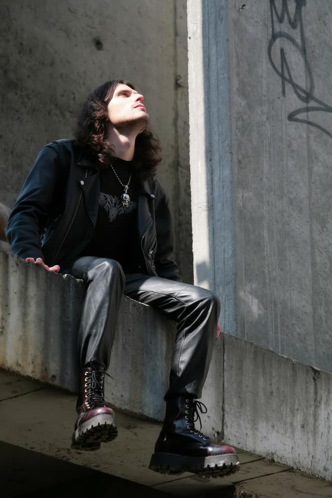 Man in a goth outfit sitting on a concrete surface.
