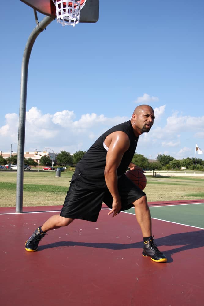 A basketball player wearing black jersey shorts and black high shoes.