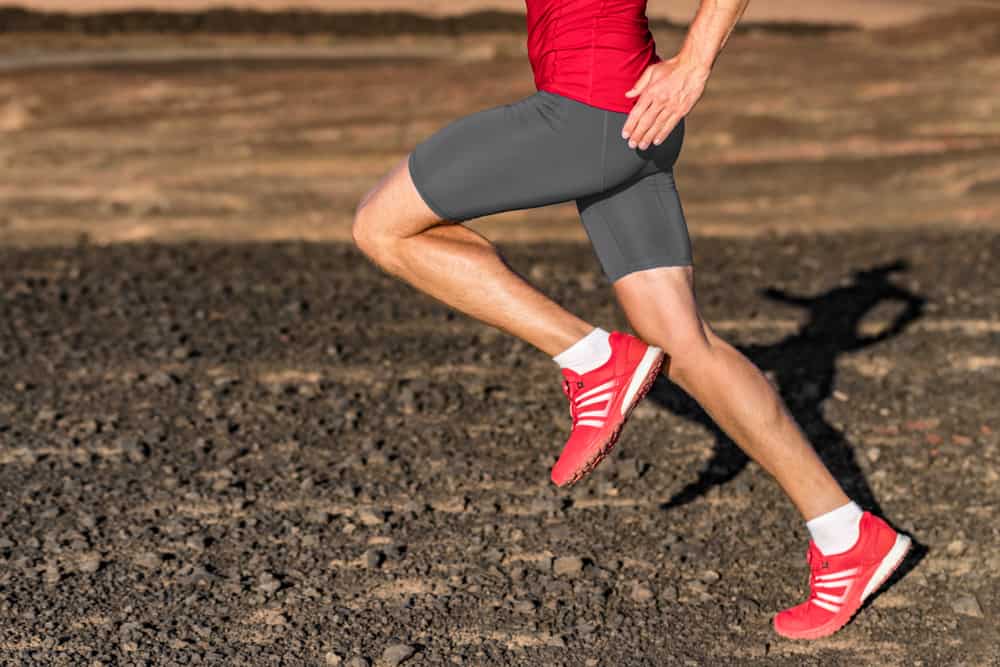 This is a close look at a man running on a rocky field while wearing a pair of compression shorts.