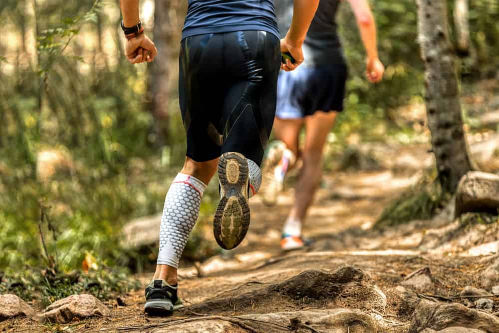 This is a close look at a man running on a forest trail wearing a pair of compression shorts.