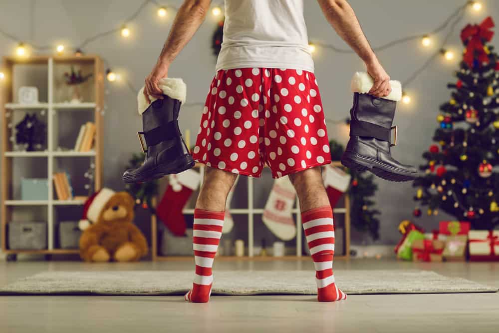 A man wearing a pair of red polka dotted shorts while holding a pair of boots.