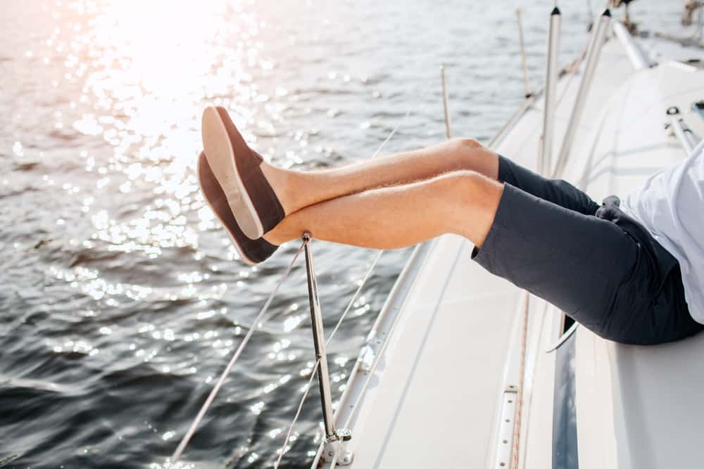 A man relaxing on a sailboat while wearing shorts and boat shoes.