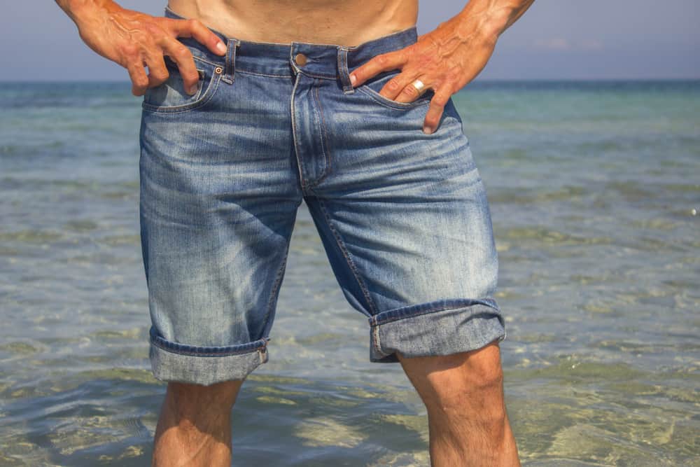 This is a close look at a man wearing a pair of jean shorts at the beach.