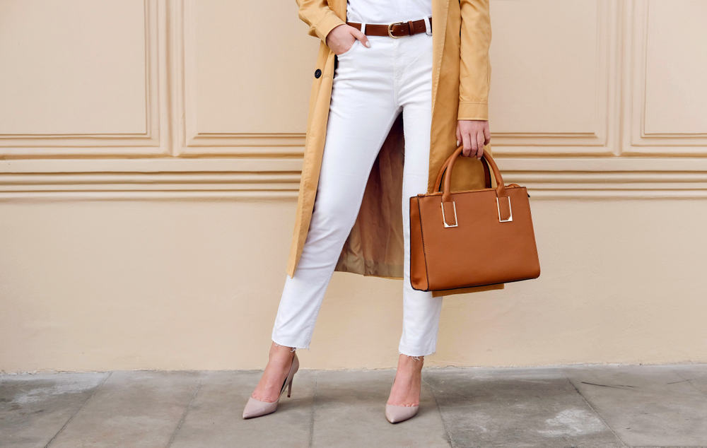 A close look at a woman wearing a pair of white jeans with long brown coat.