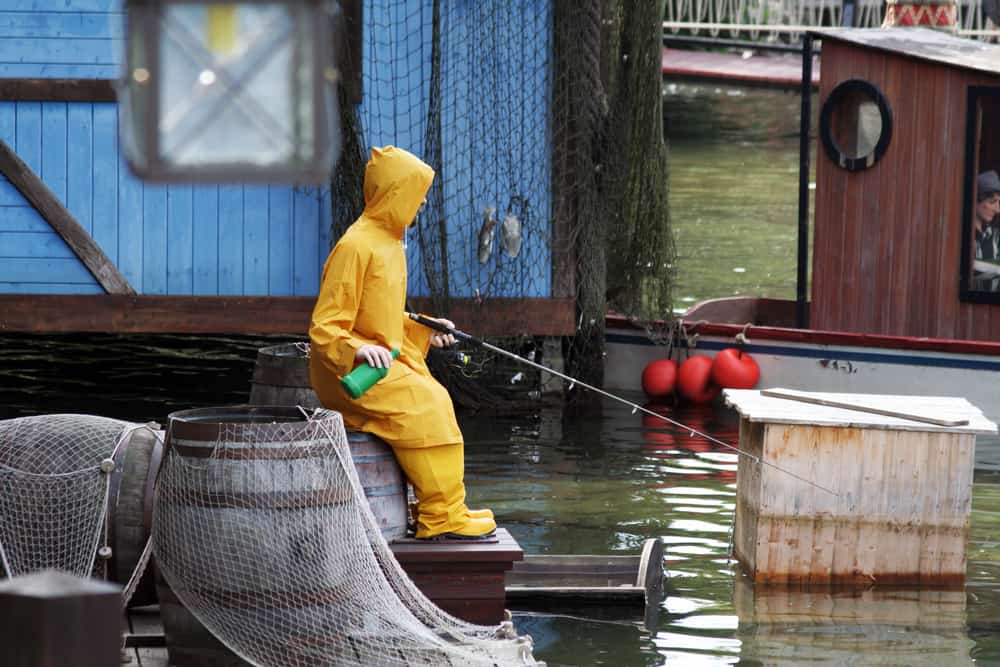 A man fishing at the docks wearing yellow rain gear.
