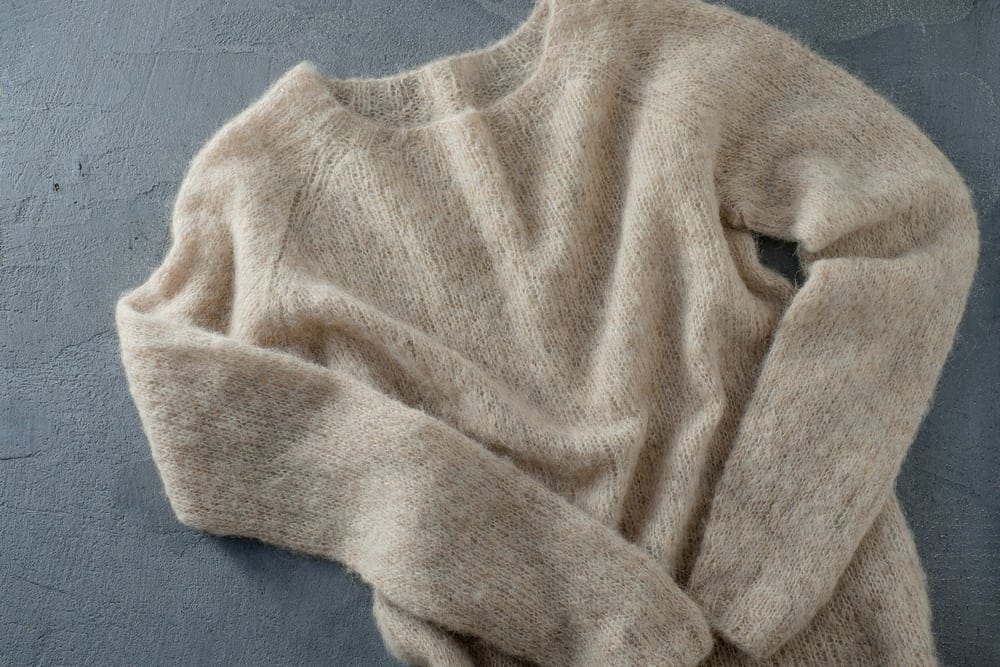 This is a close look at a pastel beige wool sweater on a concrete floor.