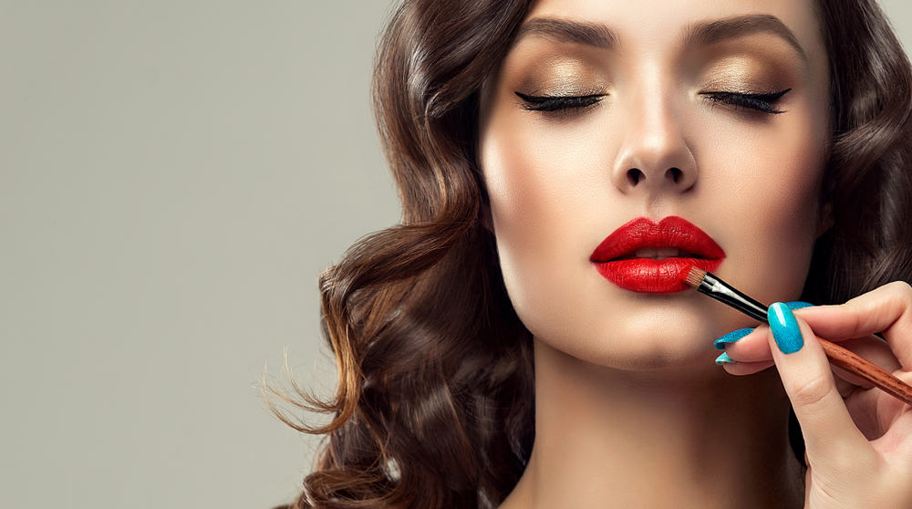 Makeup artist applying red lipstick on female model.
