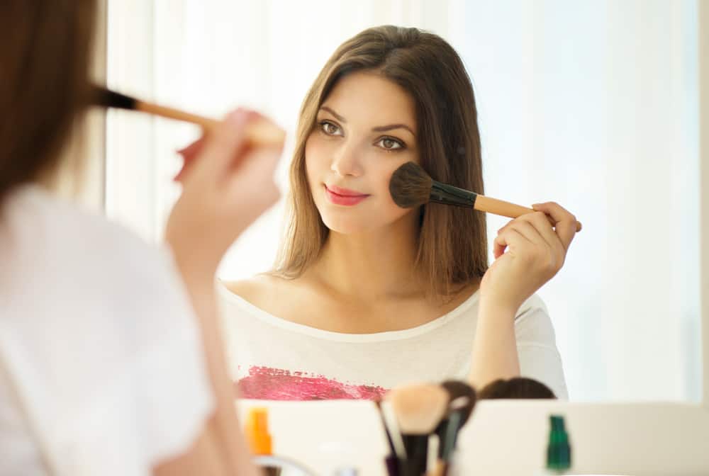 Woman applying makeup against a mirror.