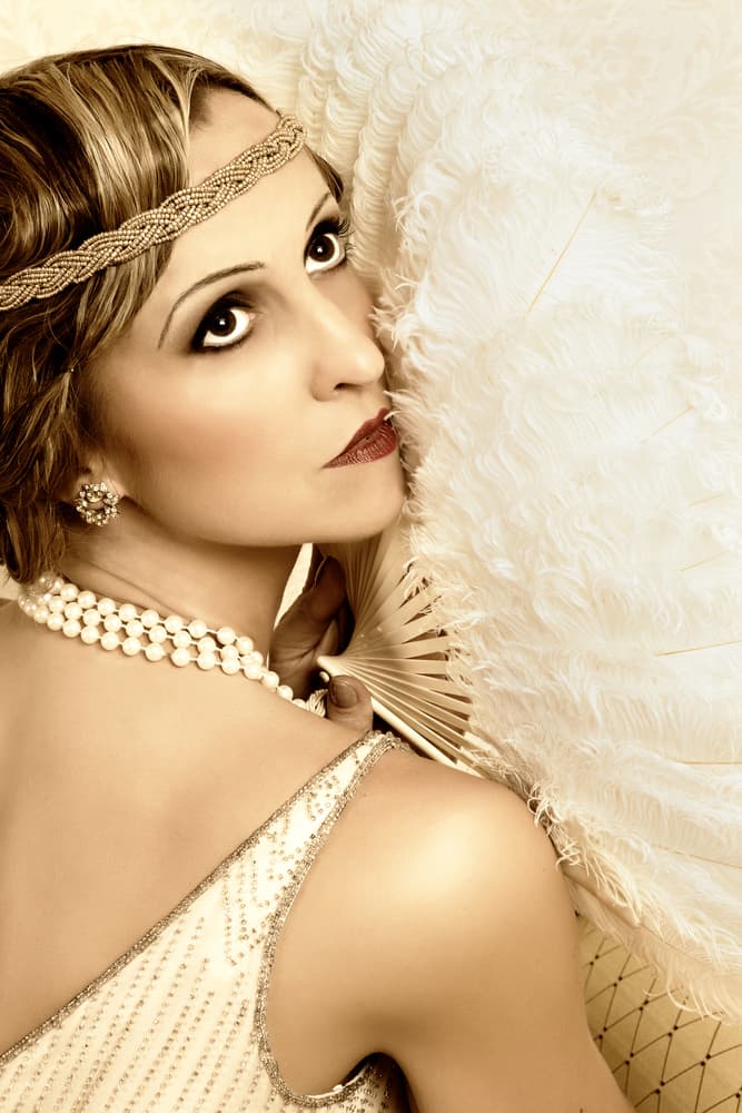 Woman with flapper dress headband holding a large, vintage fan.