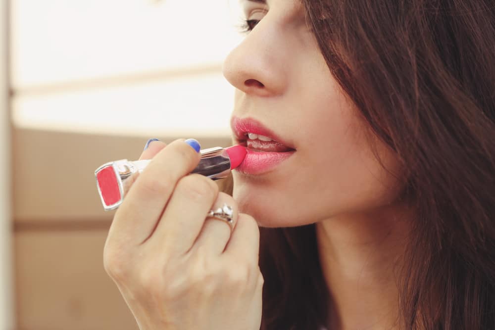 Woman applying pink lipstick.