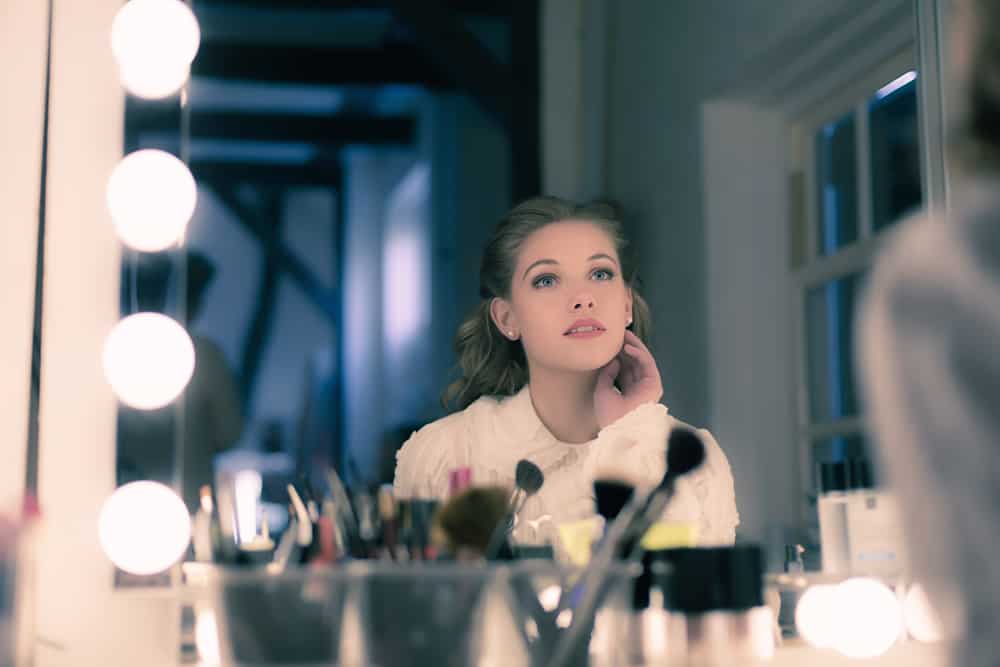 Woman with dreamy makeup looking at a vanity mirror.