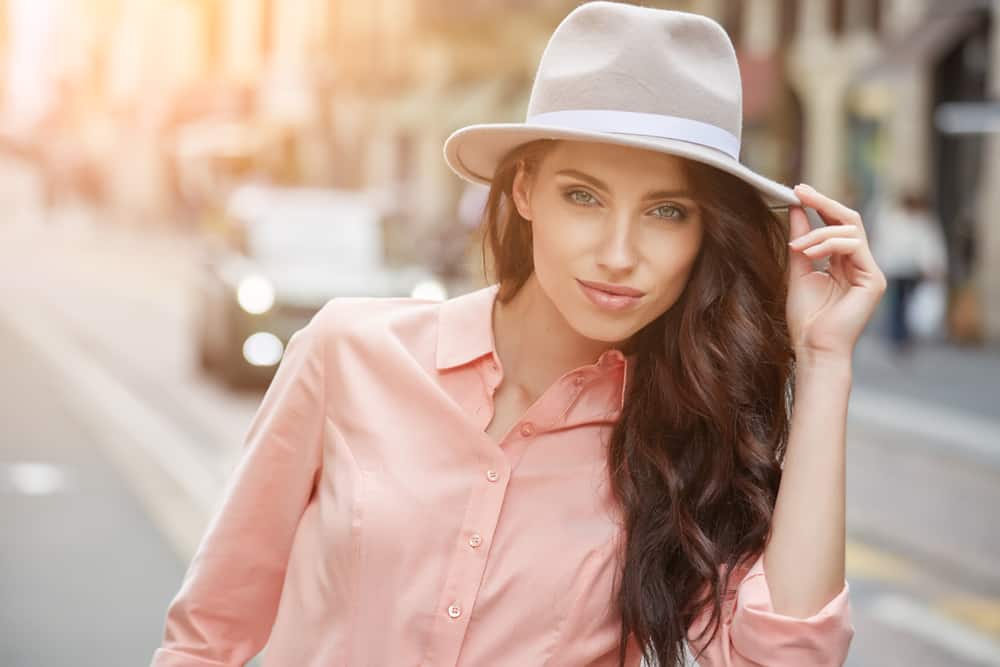 A woman wearing a pink blouse with her light gray fedora.