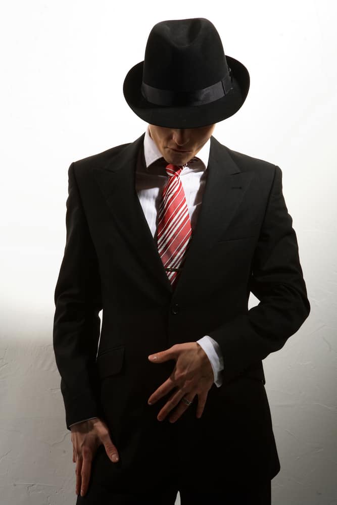 A man wearing a black fedora with his black suit.