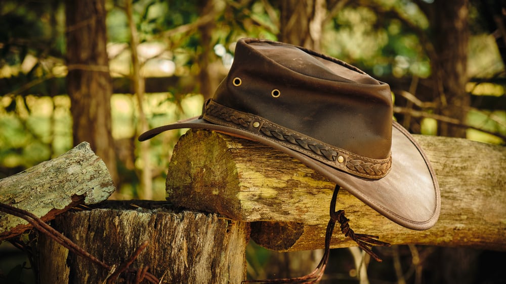 A brown leather outback hat on a log fence post.