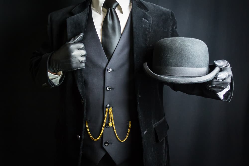 This is a man wearing a dark suit and a bowler hat in hand.