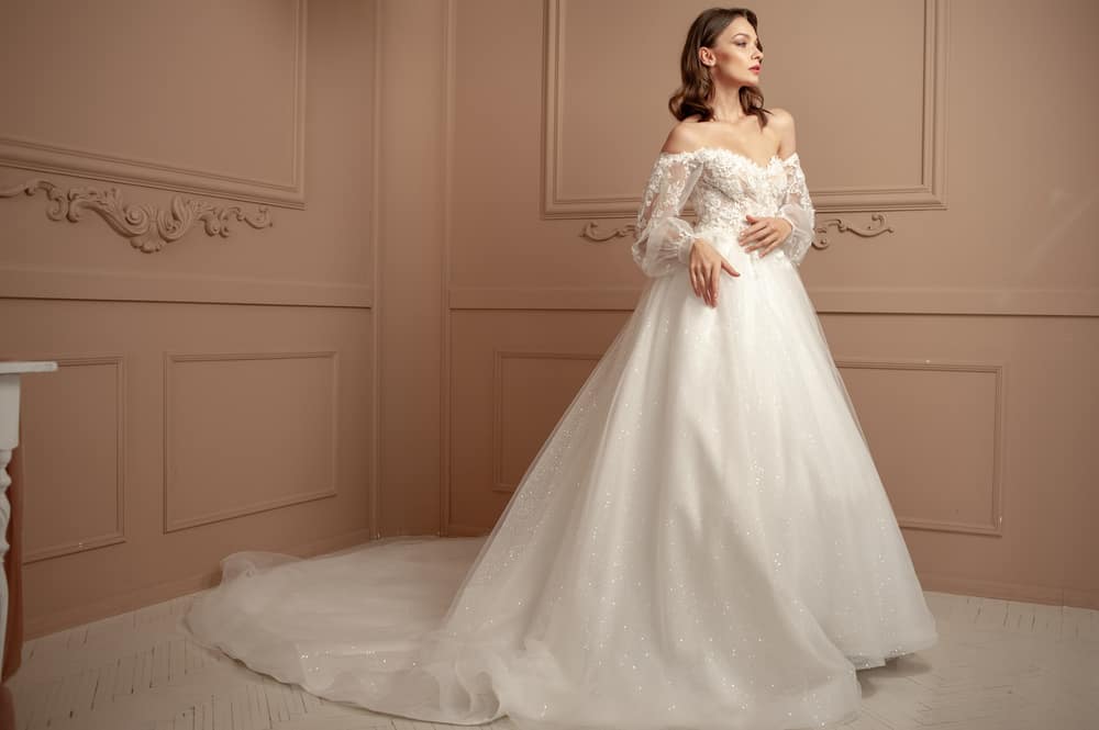 Bride in an off-shoulder wedding dress poses against the intricate wainscoted walls. 