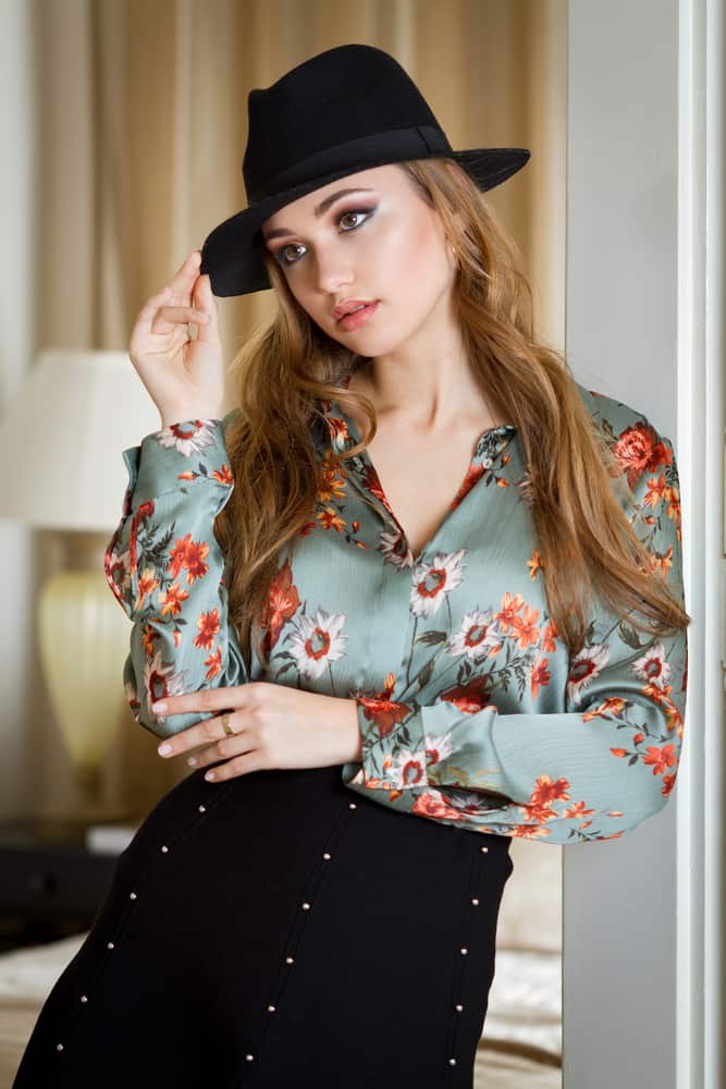 A woman wearing a floral blouse with her fedora.