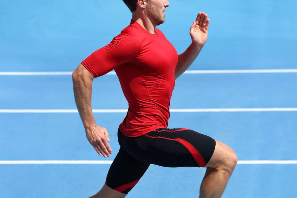 Athlete in compression clothes running on blue stadium track.