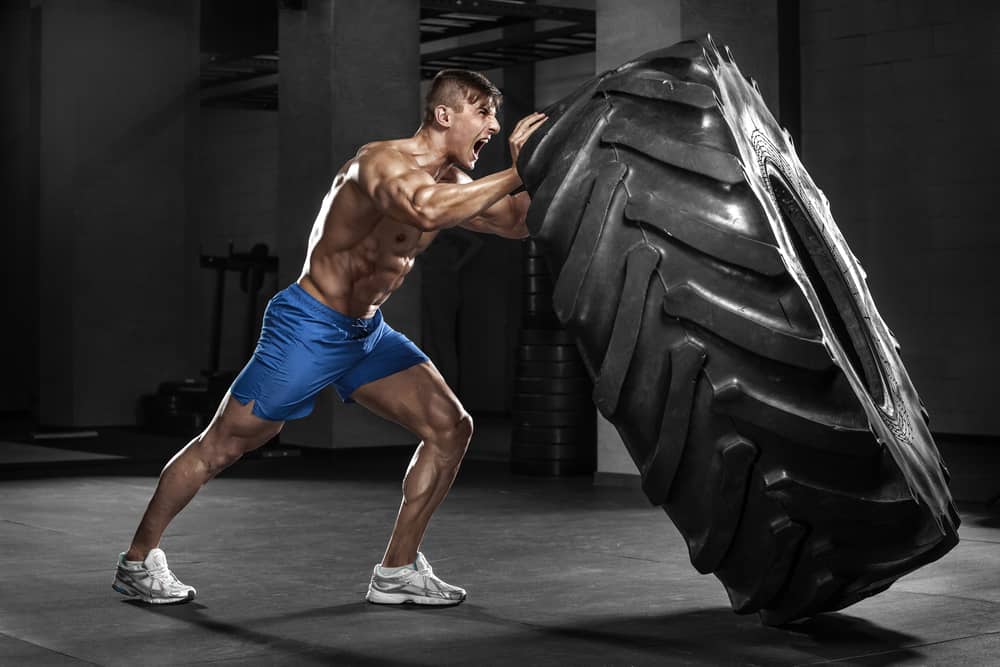 Muscular man flipping tire in a gym.