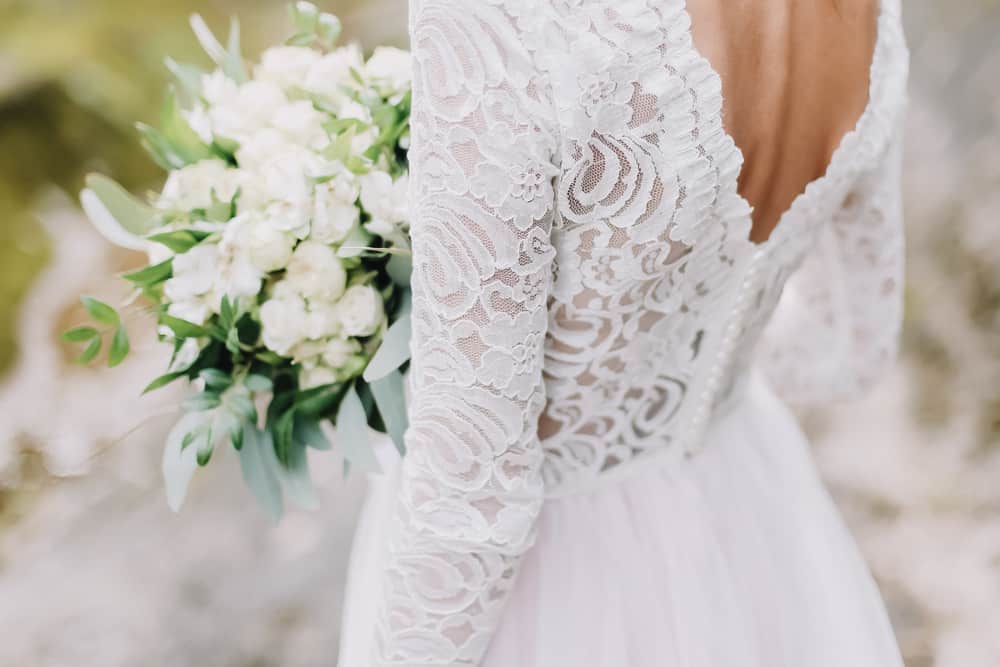 Back profile of a  bride in a lacy wedding dress holding a white bouquet.