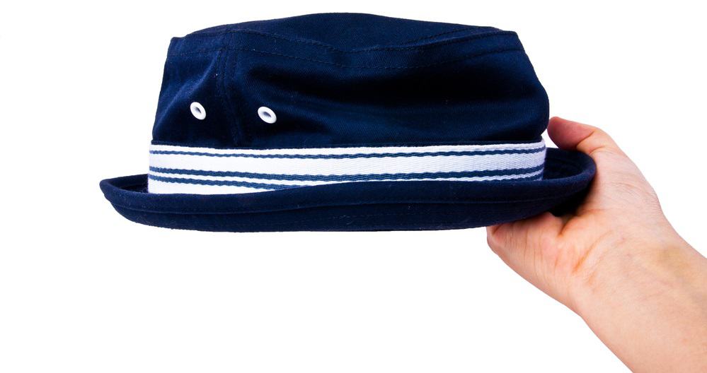 A hand holding up a vintage navy blue boater cotton fedora hat with a striped band.