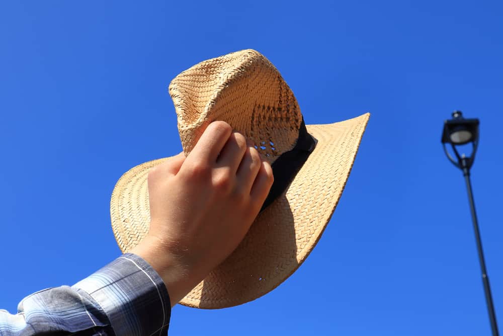 A man holding up a woven straw outback hat with a black band.