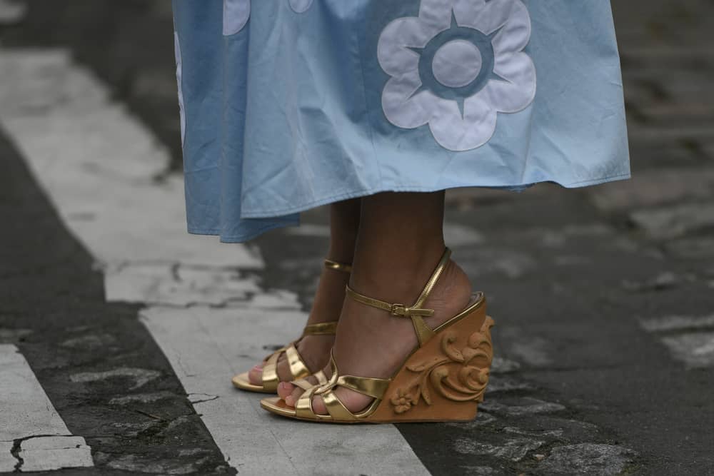 A close look at a woman wearing a pair of wedge heels that has golden straps.