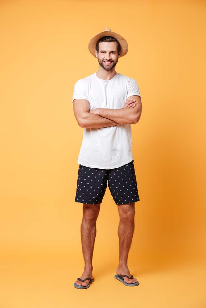 A man wearing casual slip-ons, shorts, shirt and a fedora hat.