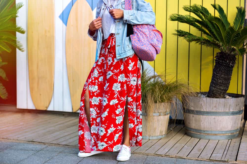 This is a close look at a woman wearing a red floral maxi skirt and a pair of white sneakers.