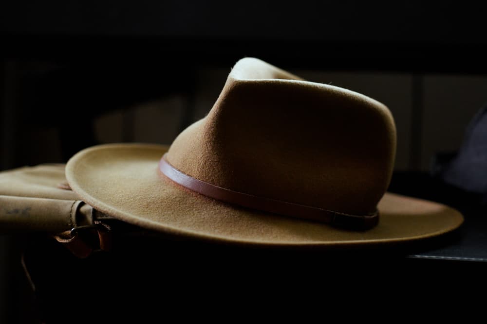 This is a close look at a brown fedora hat with a brown leather satchel.