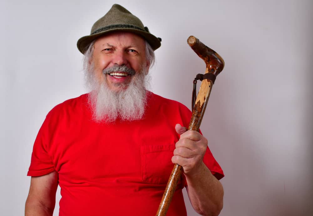 A man with a cane wearing a red shirt and a gray tylorean hat.