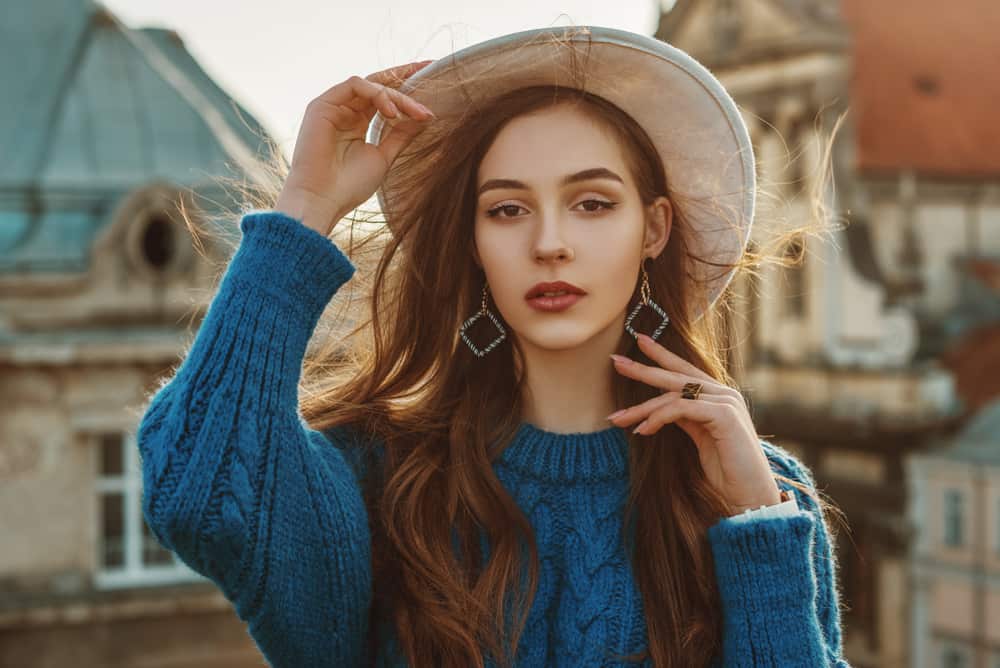 A woman wearing a blue knitted sweater with a fedora.