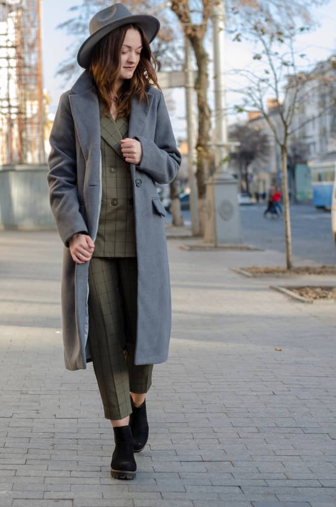A woman wearing a gray trench coat with her gray fedora.