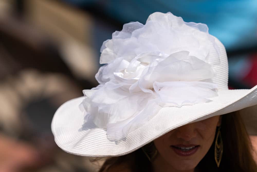 A woman wearing a white derby hat that has a floral embellishment.