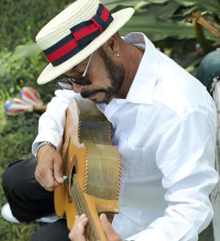 A close look at a man wearing a white boater hat while playing the guitar.