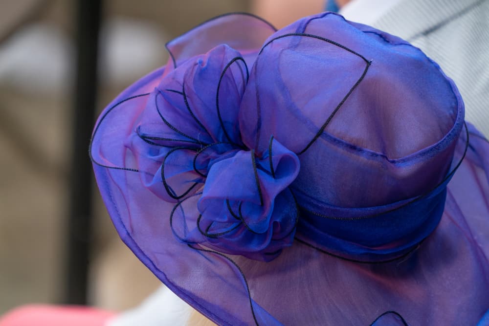 This is a woman wearing a sheer purple derby hat.