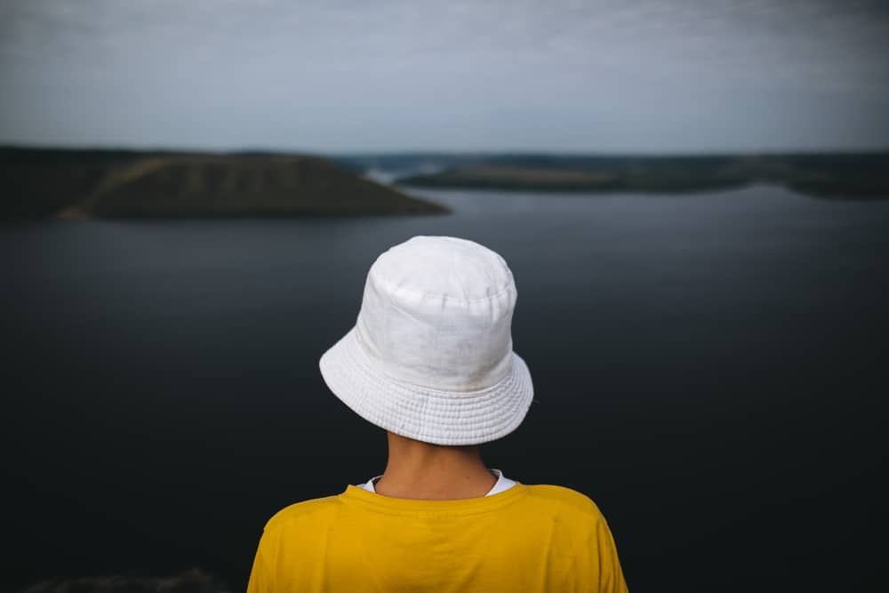 This is a view of a woman wearing a white bucket hat and yellow shirt by the river.