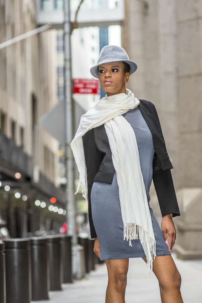 This is a woman wearing a gray dress, matching gray fedora and a white scarf.
