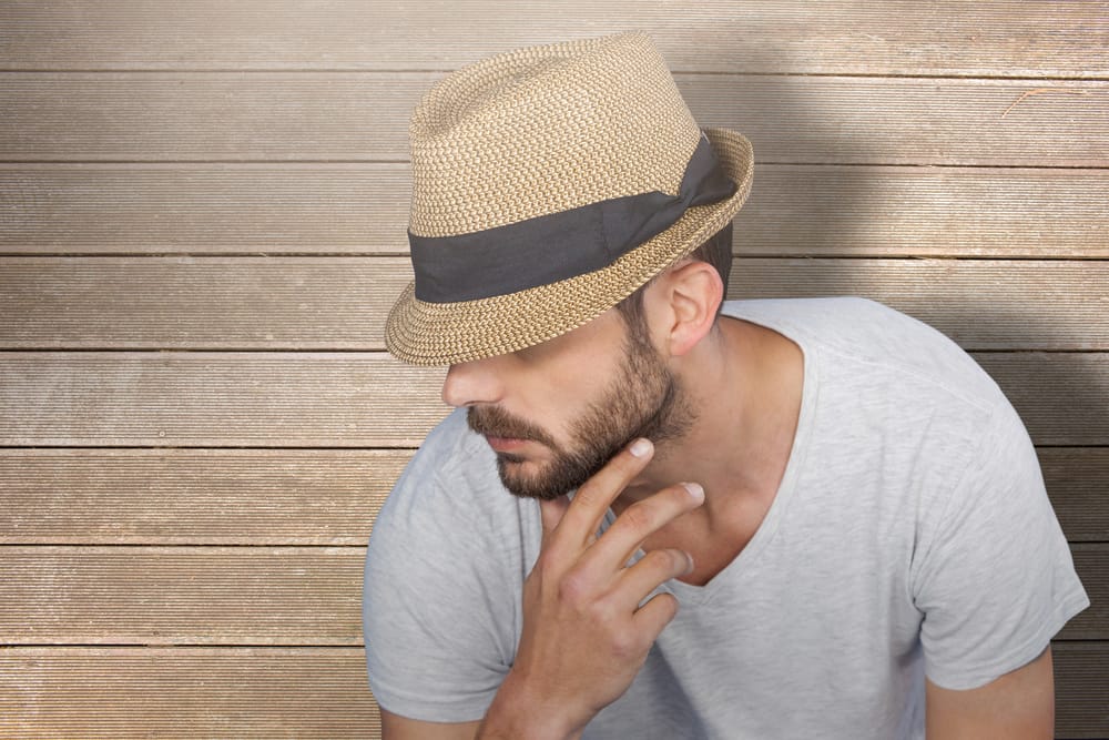 This is a close look at a bearded man wearing a gray shirt and a trilby hat.