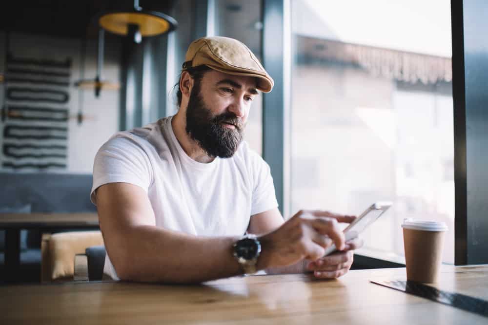This is a bearded man wearing a white shirt and an ivy cap at a coffee shop.