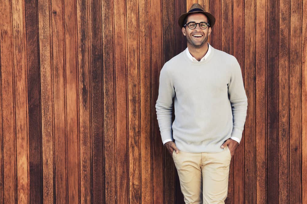 This is a man wearing a gray sweater, a pair of glasses and a trilby hat.