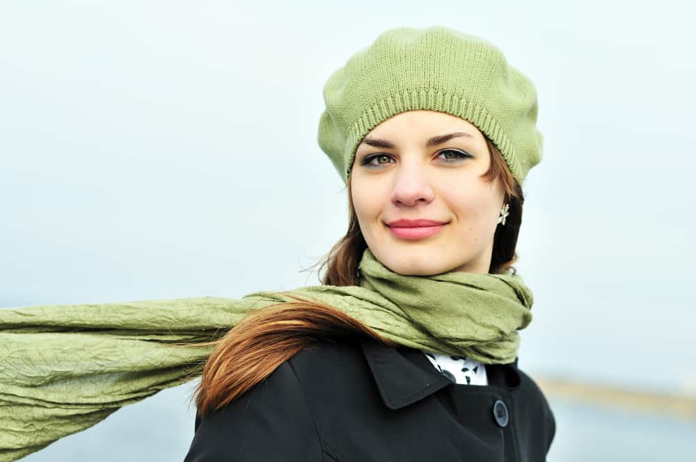 A woman wearing a green knit tam cap with matching green scarf.