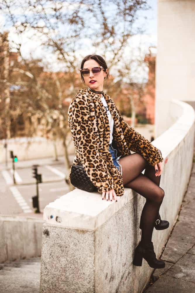 This is a fashionable woman wearing a leopard jacket, a denim skirt and leggings underneath.